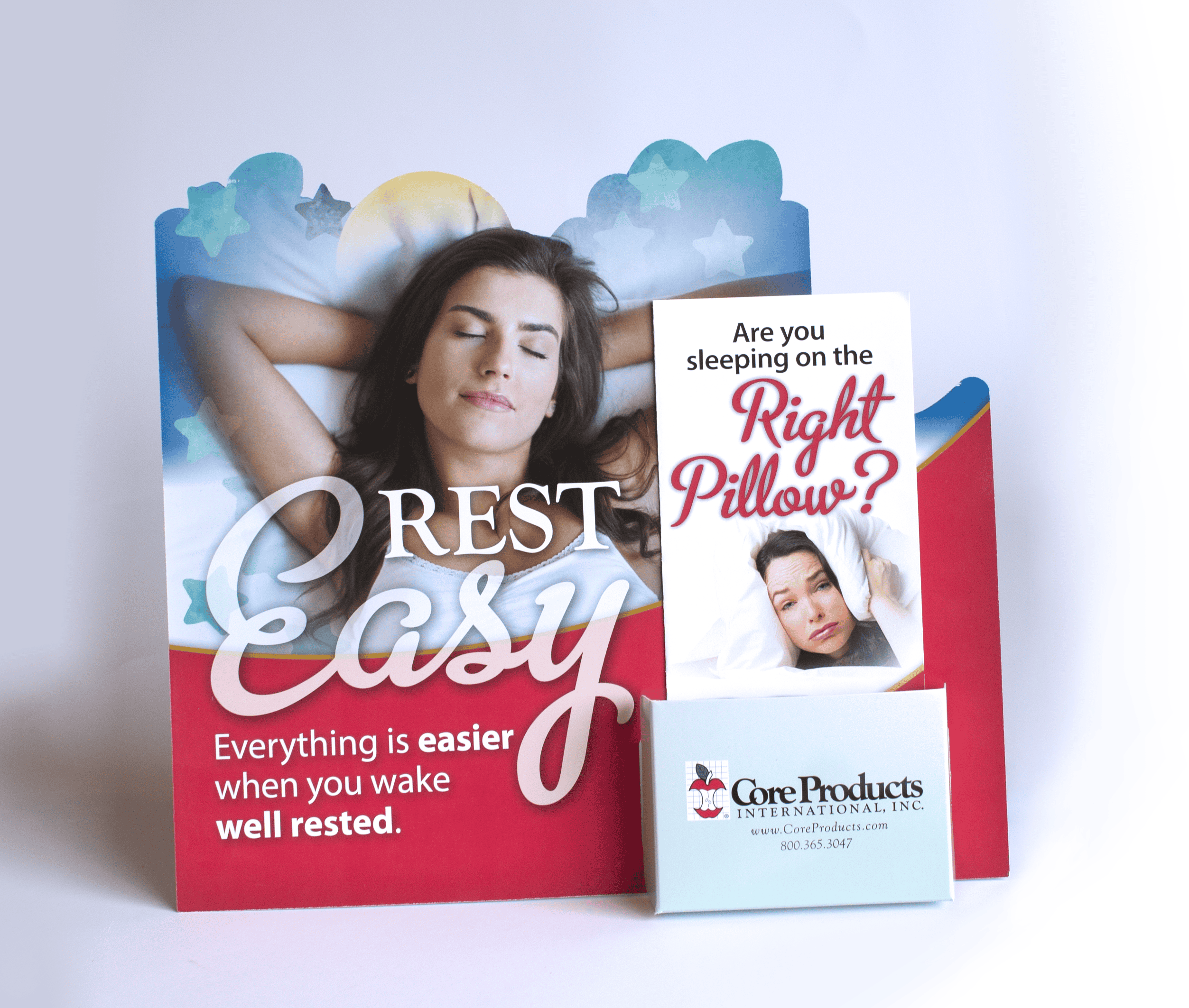 Display stand for Core Products International, Inc. featuring the headline "Rest Easy" with an image of a relaxed woman lying in bed. The tagline reads, "Everything is easier when you wake well rested." A brochure next to it asks, "Are you sleeping on the right pillow?" with an image of a woman appearing uncomfortable, implying pillow-related sleep issues. There is also a small box with the Core Products logo and contact information.