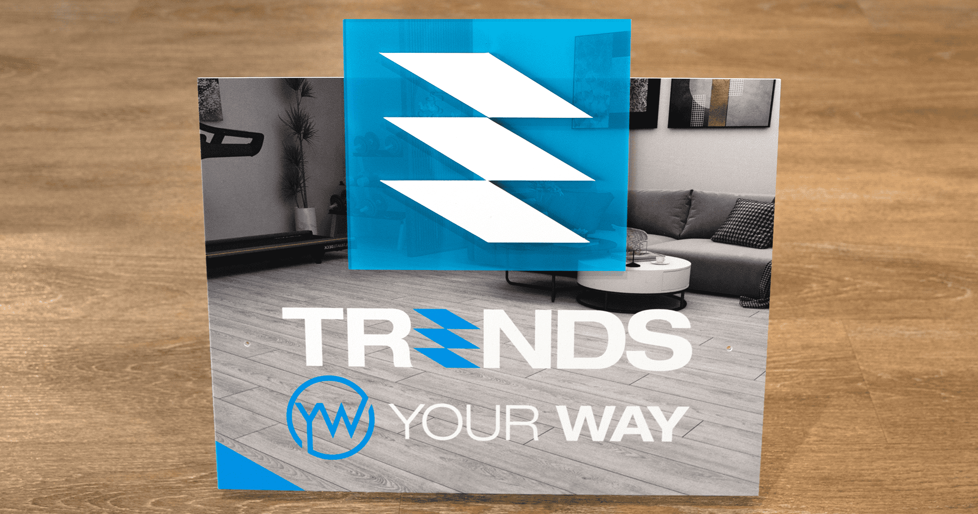 Display for Trends Your Way featuring a modern logo with bold white and blue geometric elements. The background shows a sleek living room interior with wood flooring and contemporary furniture. The text "TRENDS YOUR WAY" is displayed prominently at the bottom, with the "Your Way" portion incorporating a stylized circular icon.