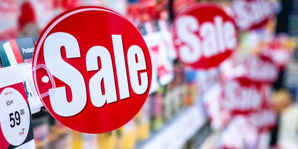 Bright red sale signs hanging in a retail environment, highlighting discounted products with bold white text.