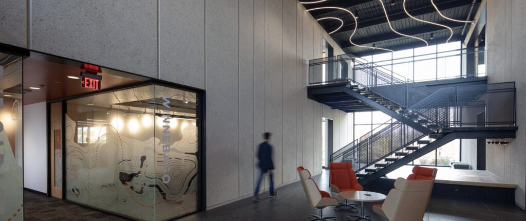 Modern lobby at Thysse's Oregon, WI headquarters, with a staircase, glass-walled meeting room, and artistic ceiling lighting.