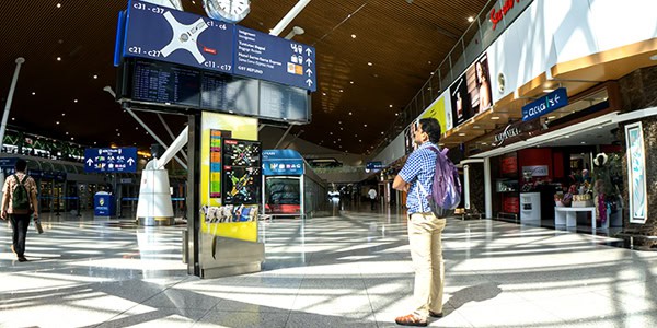 A man in an airport terminal looking up at wayfinding signage, including flight information and directions.