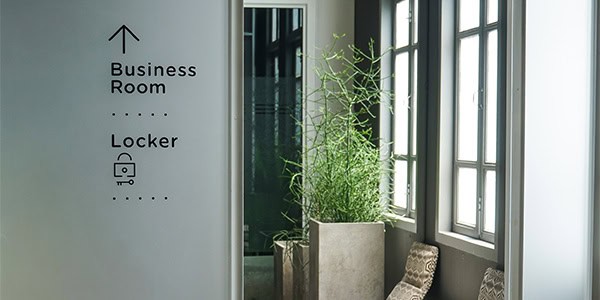 Interior wayfinding signage showing directions to a business room and locker area, with simple black icons on a sleek white wall.