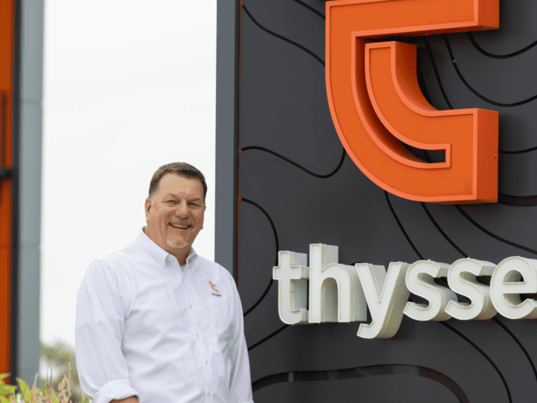 Dean Bott, President and General Manager of Thysse, standing in front of a Thysse sign featuring the company logo and name.