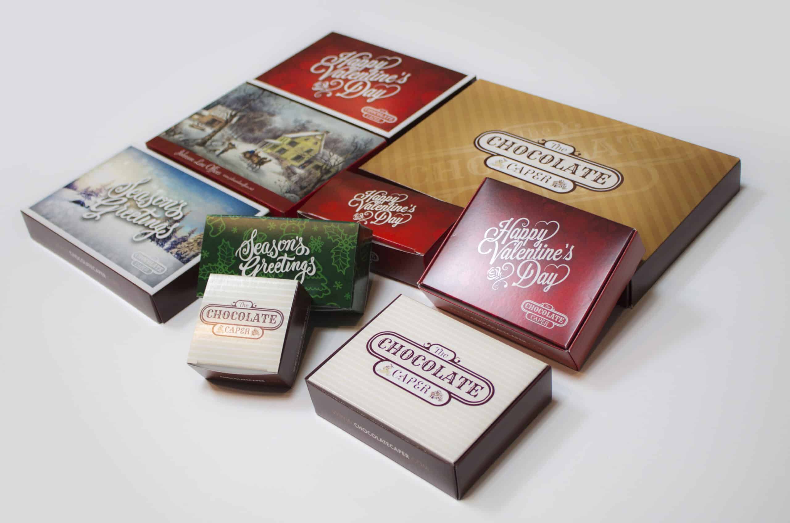 Chocolate Caper - Promotional Boxes A collection of custom-branded chocolate boxes for The Chocolate Caper, featuring seasonal packaging designs for holidays like Valentine’s Day and Season’s Greetings. The packaging incorporates warm tones, elegant typography, and rich textures, emphasizing a premium, gift-ready presentation.