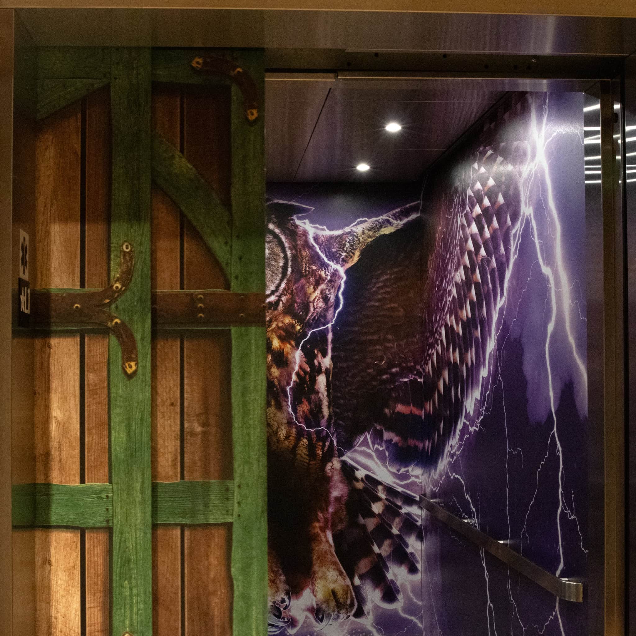 Elevator doors at Epic’s Verona campus with a rustic green and wood plank wrap partially opened to reveal an owl-themed interior graphic.