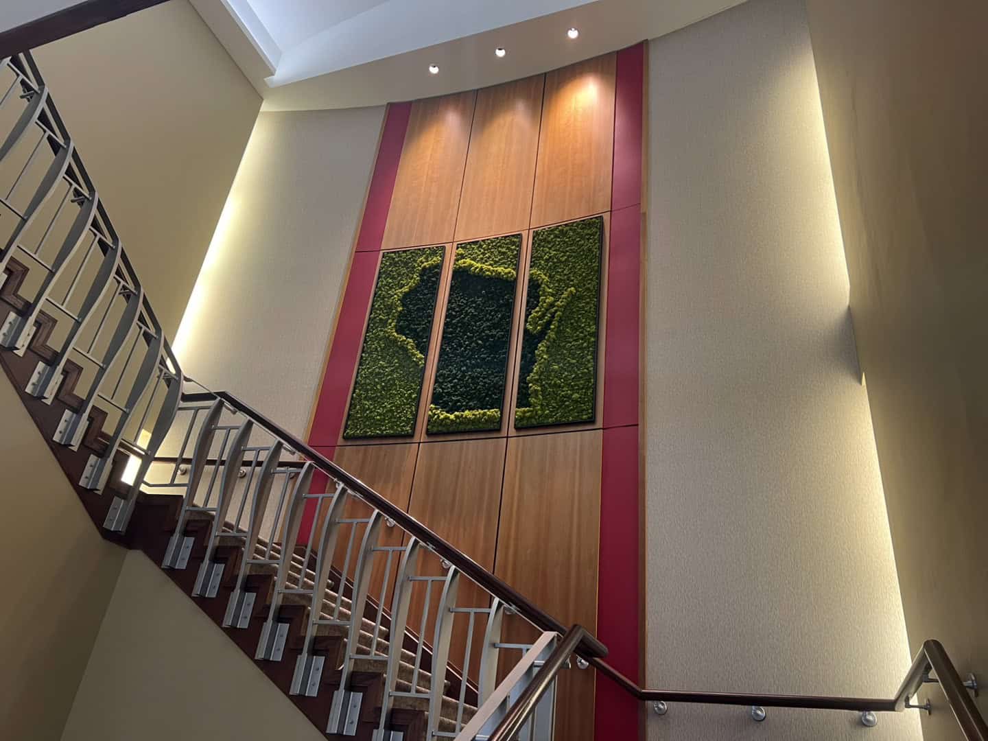 Moss art installation viewed from a stairwell, showcasing a three-panel display of Wisconsin’s outline made with green moss against a wooden wall.