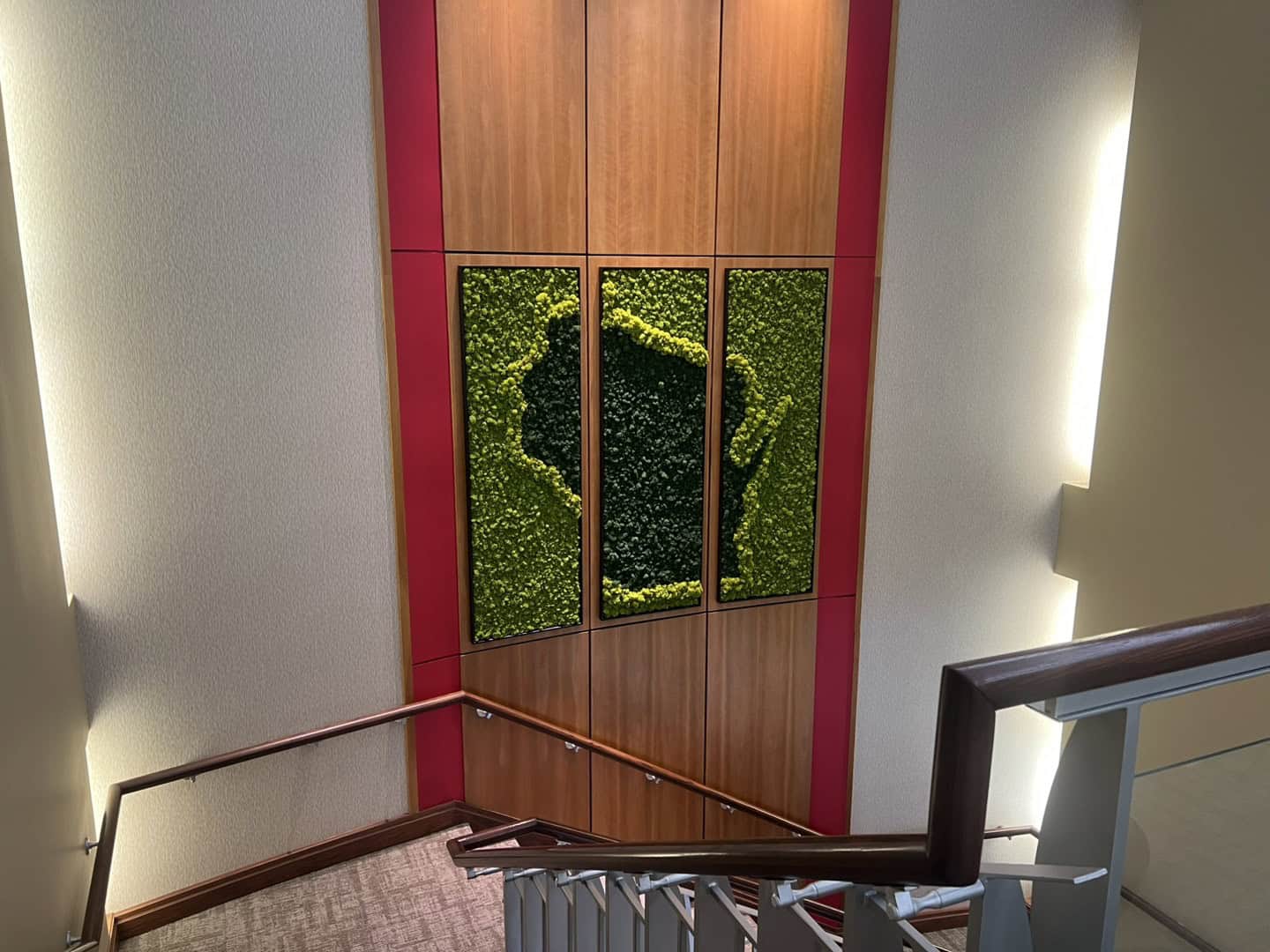 Overhead angle of moss wall installation at the stair landing, highlighting the textured moss design and clean wood and red trim detail.