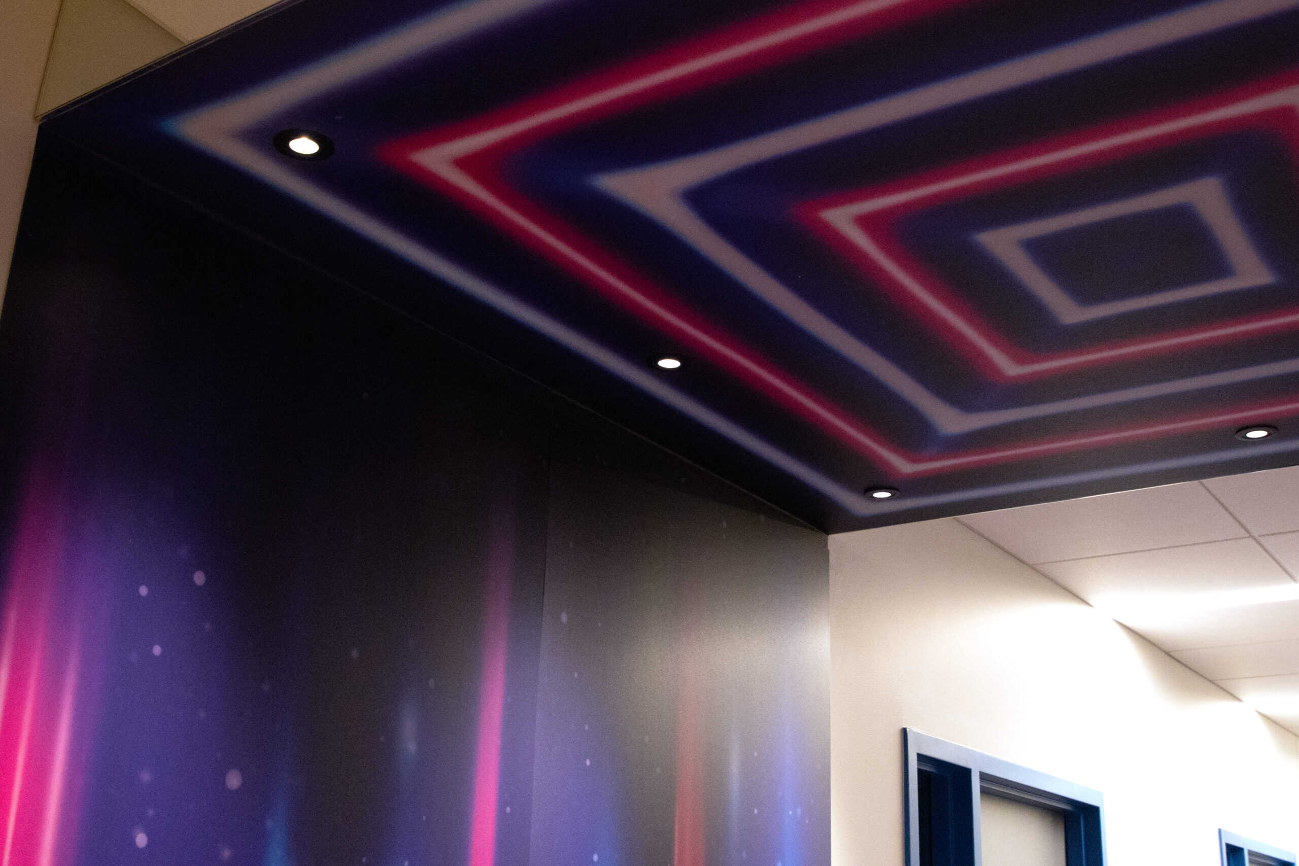 A glowing ceiling mural with concentric neon rectangles in shades of pink, blue, and white, part of a themed hallway at a corporate software company campus.
