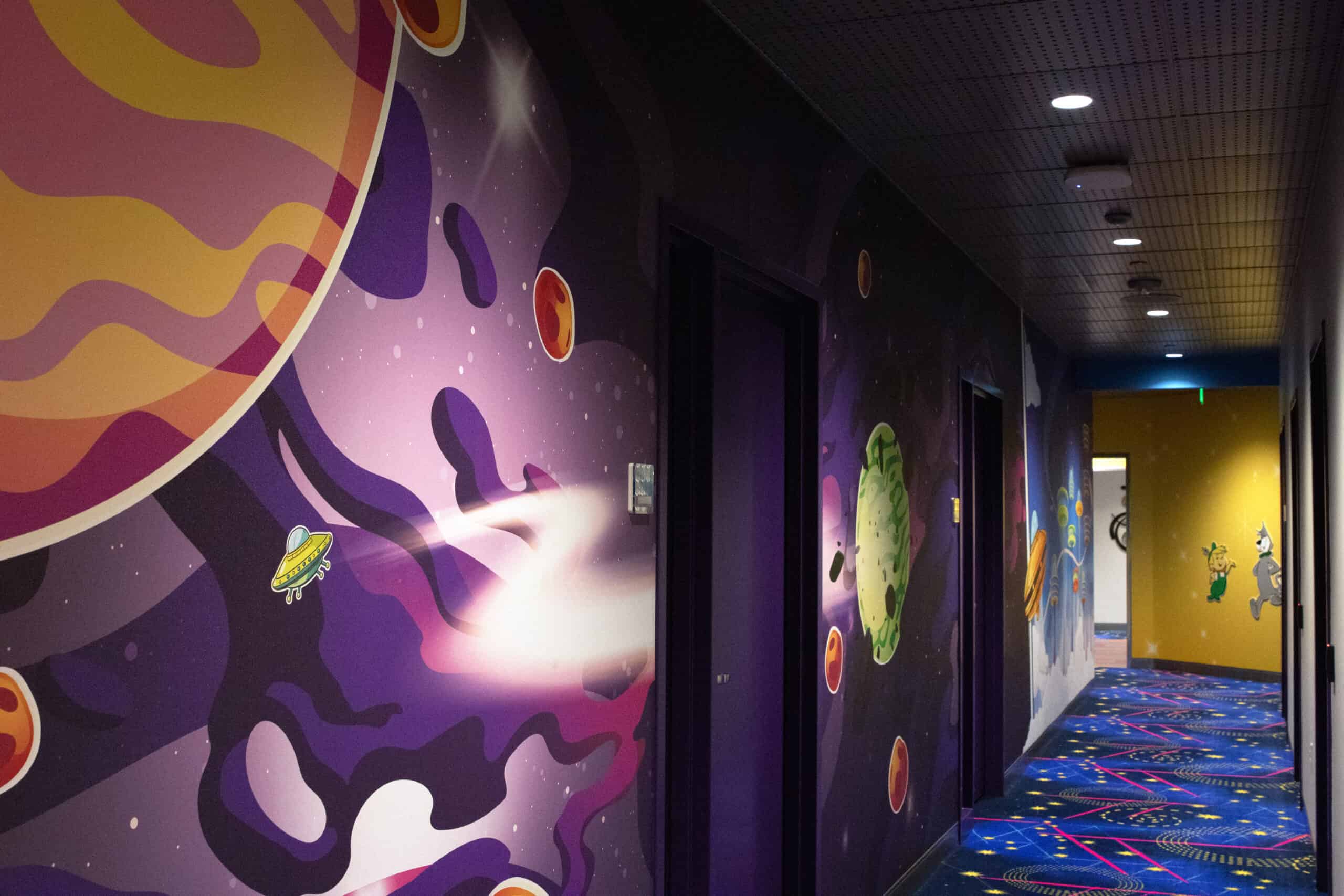 A vibrant hallway mural featuring illustrated planets, asteroids, and UFOs in a cartoon space scene at a corporate software company campus.