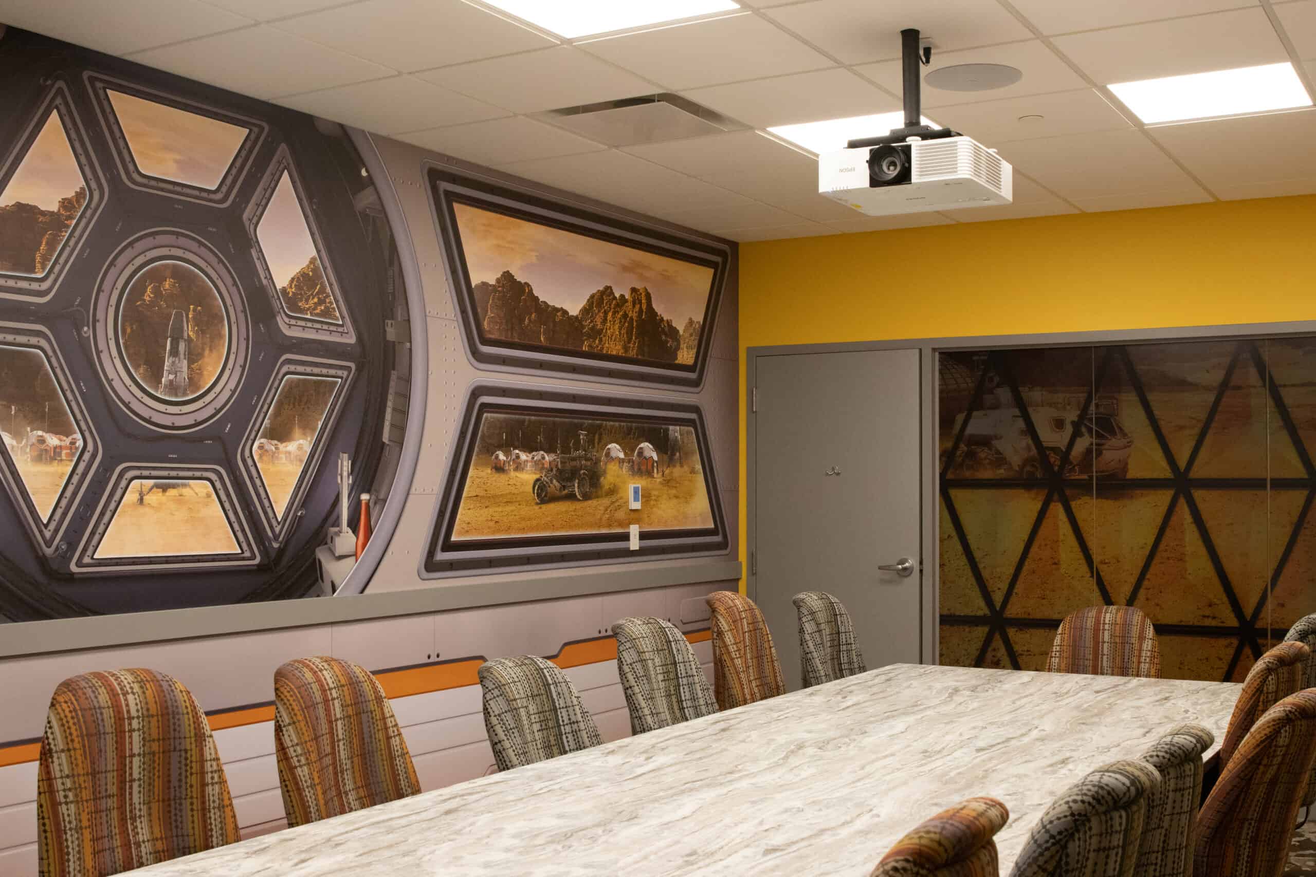 A space-themed conference room designed to resemble a spacecraft interior, with wall graphics showing views of a sci-fi desert planet and a control panel aesthetic surrounding the seating area.