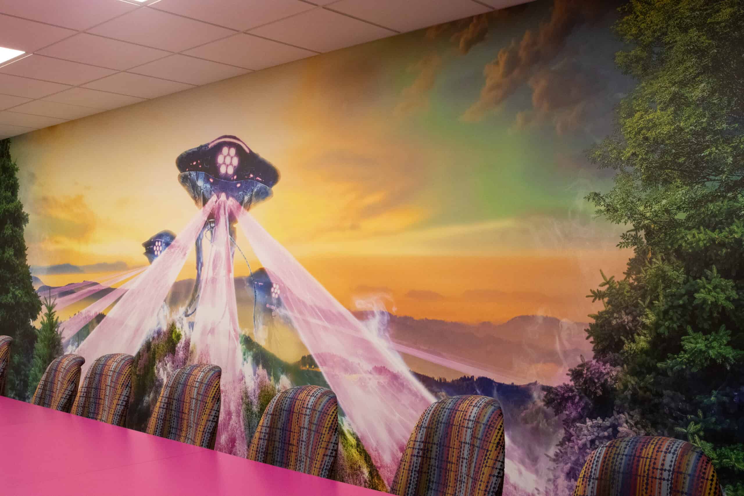 A brightly colored conference room with a vibrant mural of alien spaceships beaming colorful lights onto a surreal landscape at sunset, paired with a hot pink conference table and multicolored upholstered chairs.