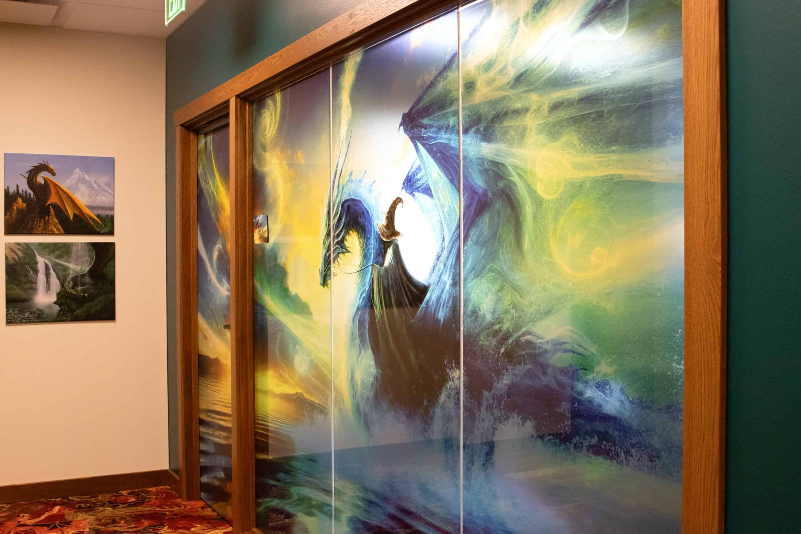 A fantasy-themed glass conference room with a dramatic mural of a wizard riding a blue dragon, framed by swirling magic and crashing waves, creating a cinematic visual centerpiece.