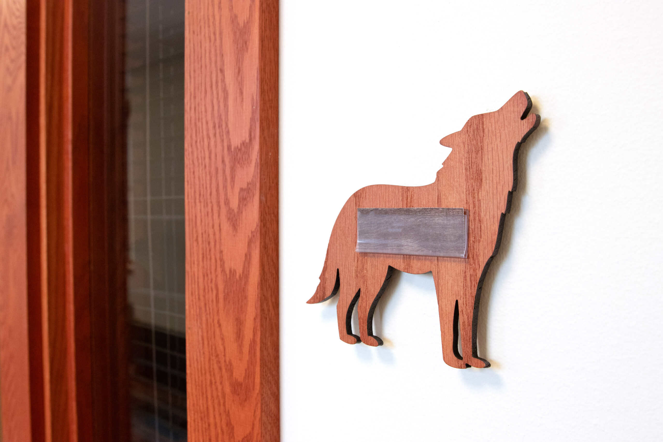 Red wood cutout of a howling wolf used as a room sign, installed on a white wall next to a door with a wooden frame.