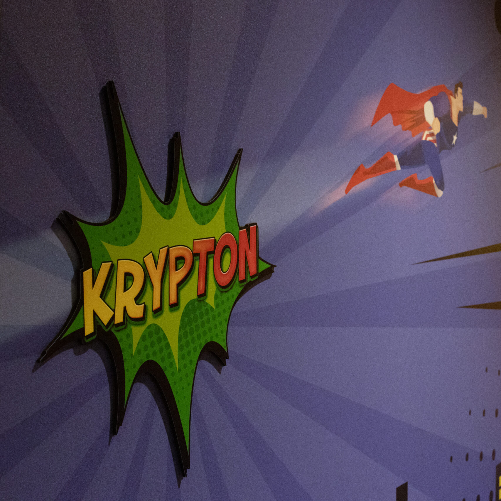 Comic-style wall mural with a flying superhero and a bold “KRYPTON” room sign designed in a bright green explosion bubble.