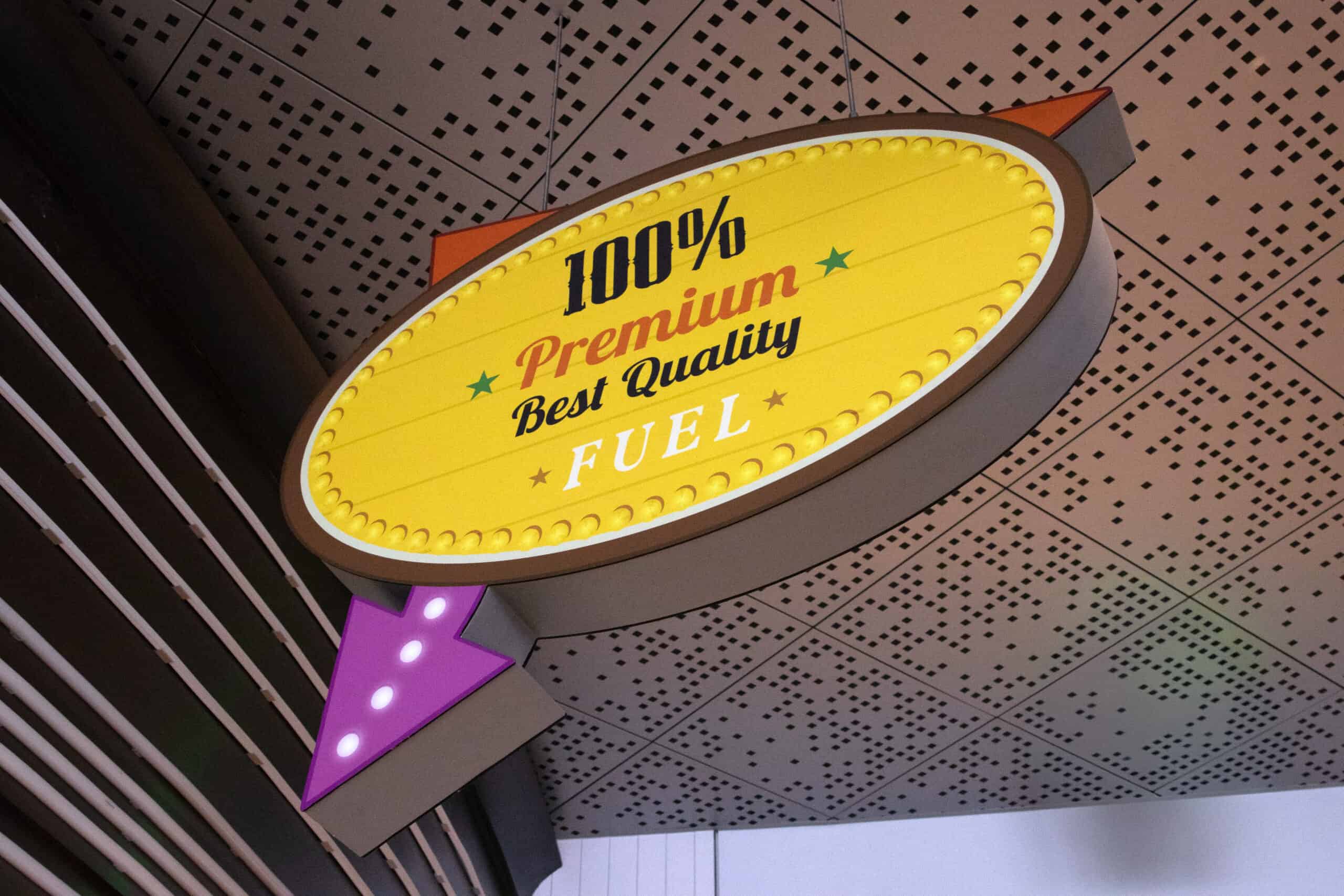 Overhead arrow-shaped sign resembling a retro gas station marquee, reading “100% Premium Best Quality Fuel” in colorful type.
