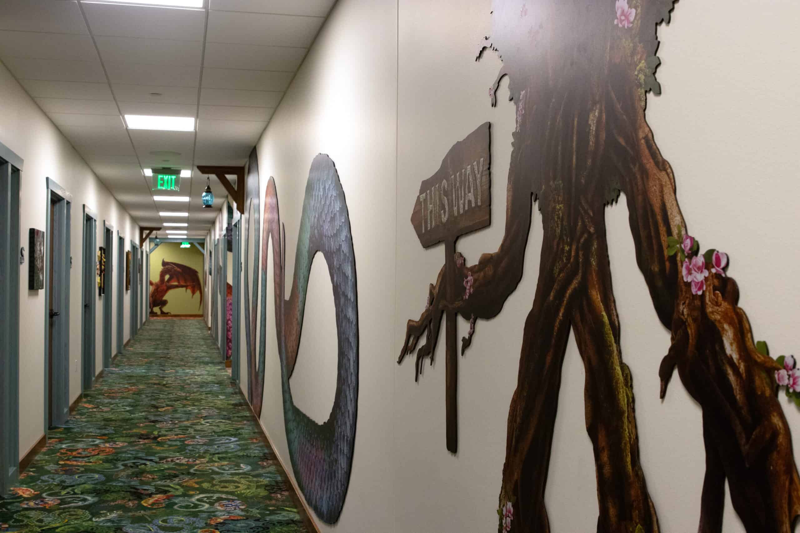 Fantasy-themed hallway with a “THIS WAY” sign held by a tree character and walls decorated with a giant coiled serpent and forest motifs.