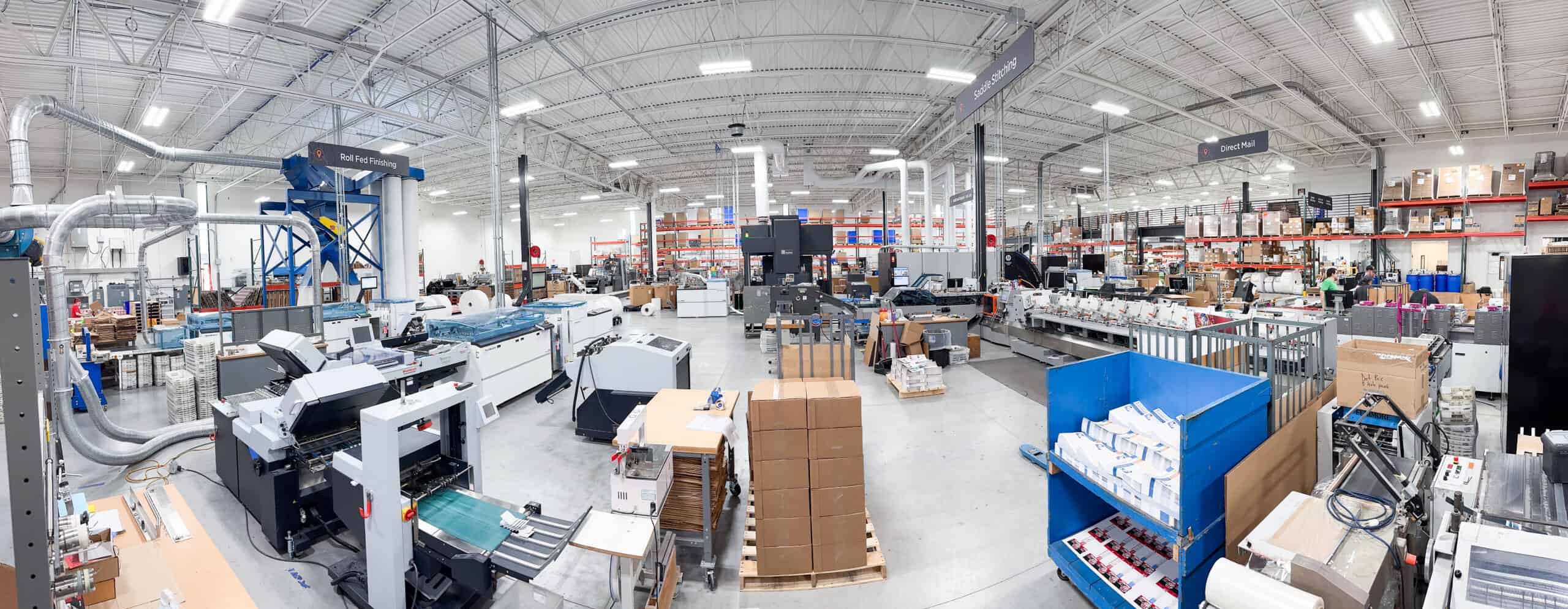 Wide-angle view of Thysse’s headquarters production floor showing the Direct Mail department. The HP A2200 roll-fed inkjet press is visible on the left, alongside finishing equipment and stacks of printed materials. Overhead signage marks different production zones, including “Roll Fed Printing,” “Digital Inkjet,” and “Direct Mail.” Workers and shelving units with organized boxes appear in the background under bright warehouse lighting.