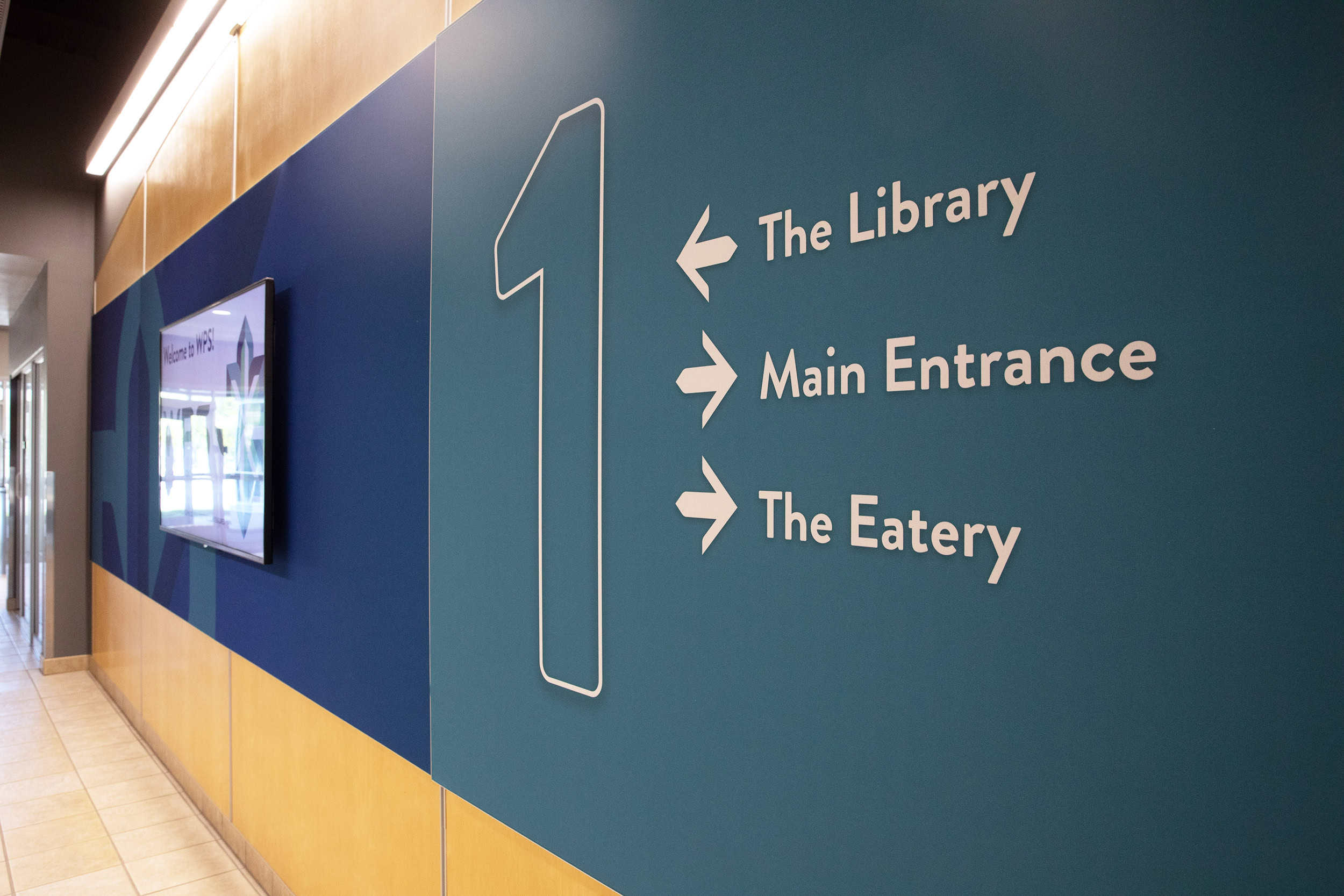 Large numeral 1 with wayfinding signage for library, main entrance, and eatery at WPS headquarters