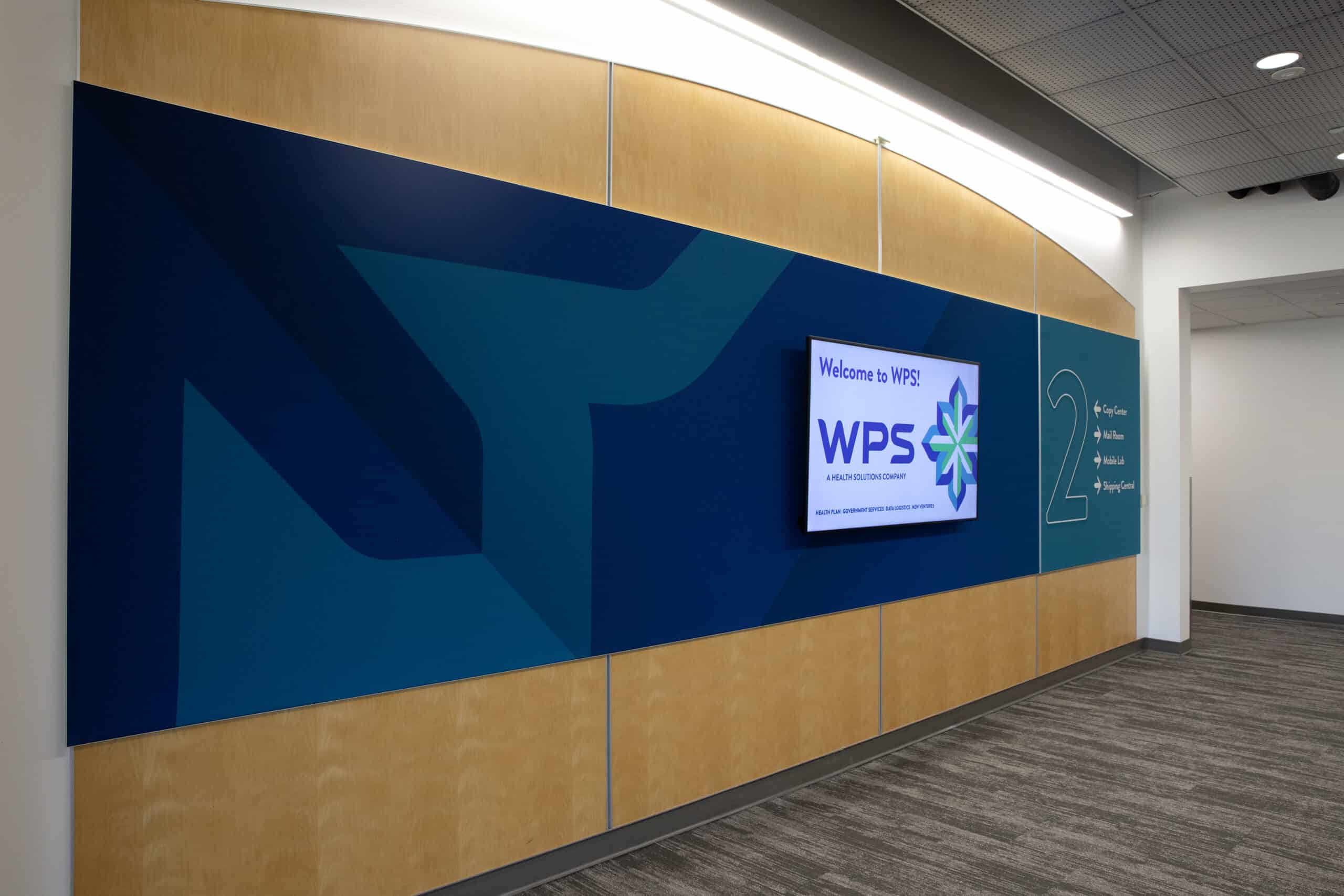 Branded wayfinding wall at WPS headquarters with monitor display and large numeral 2 directing to copy center, mail room, media lab, and shipping.