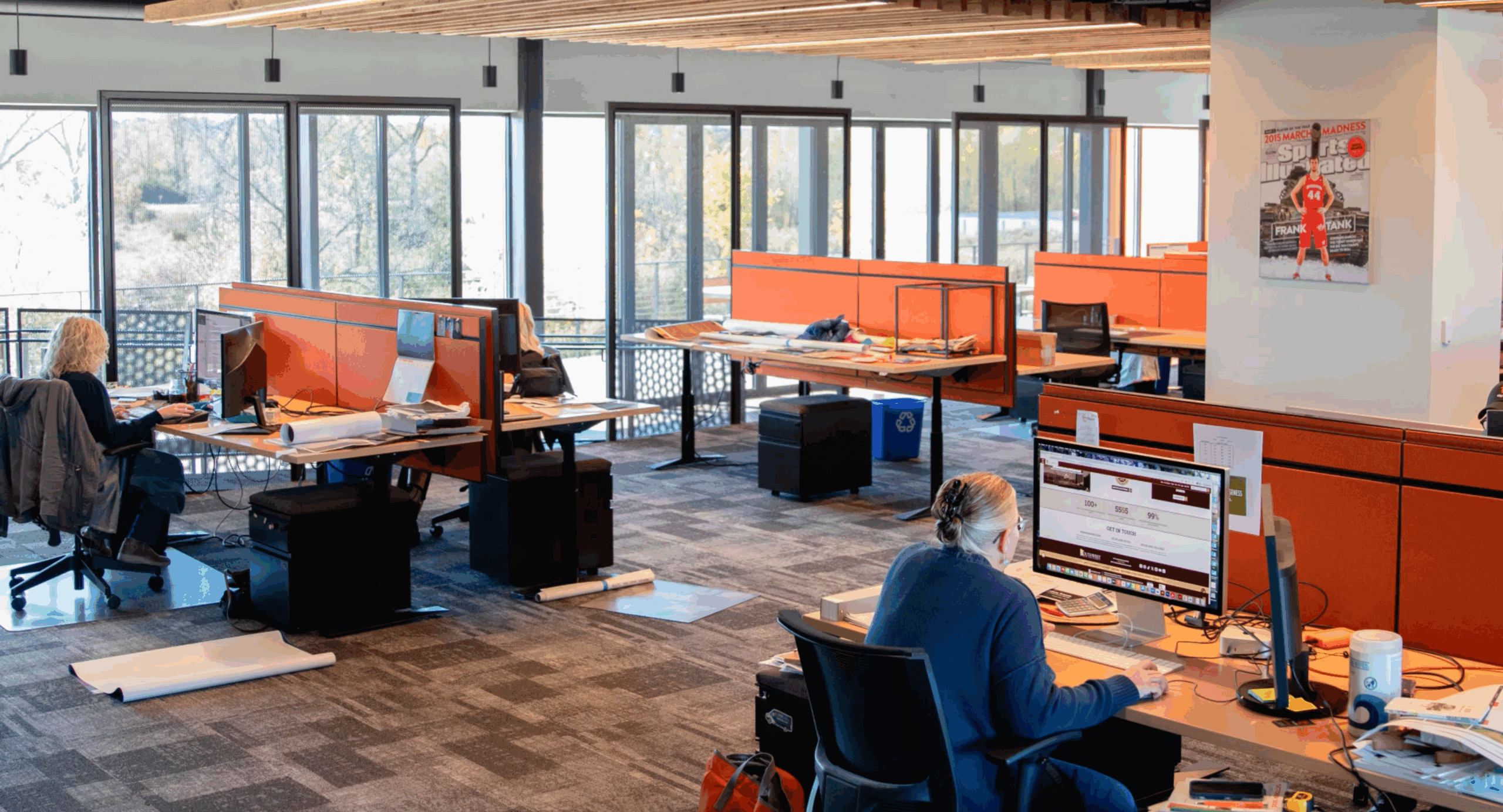 Open office workspace in Thysse’s Creative Services area, featuring bright orange cubicles, natural light from large windows, and employees working at desks.