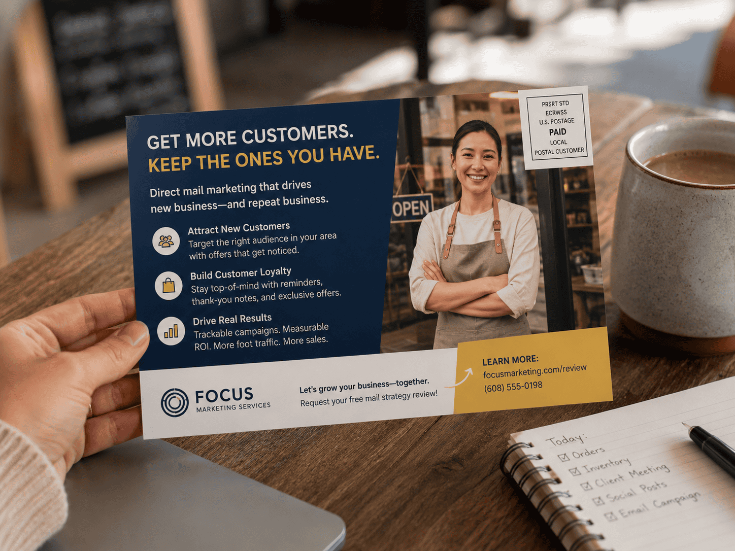 A local business owner holds a marketing postcard about using direct mail to attract new customers and retain existing customers in a cozy café workspace.