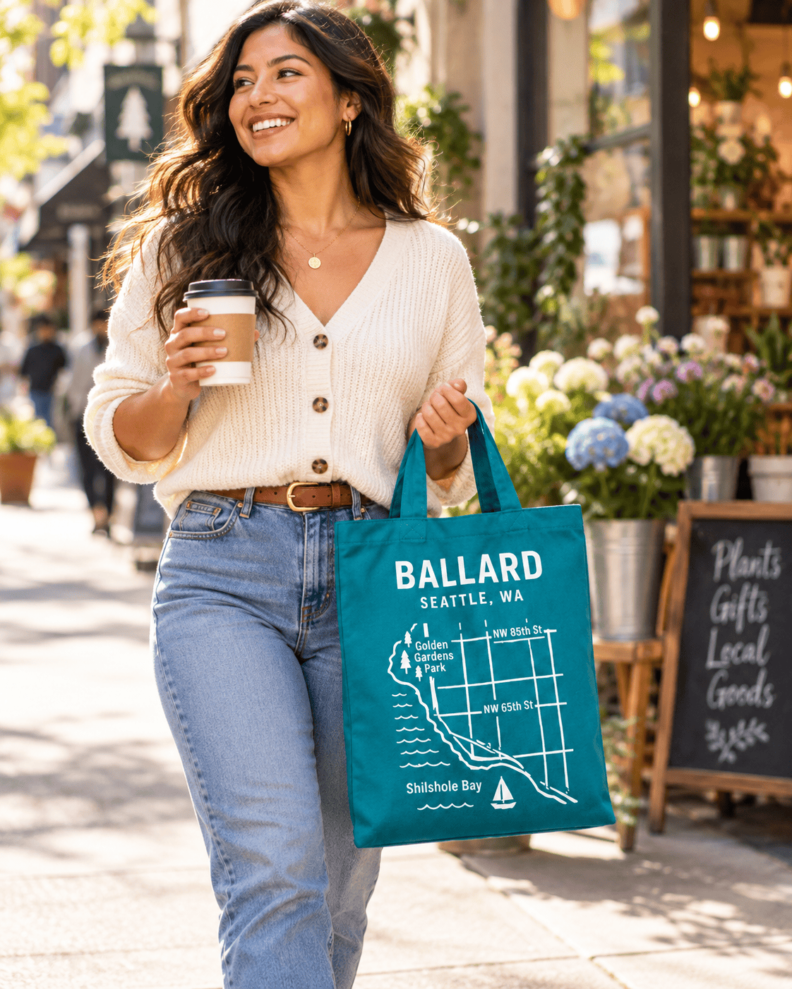 Shopper carrying a Ballard neighborhood tote and coffee while walking through a local retail district.